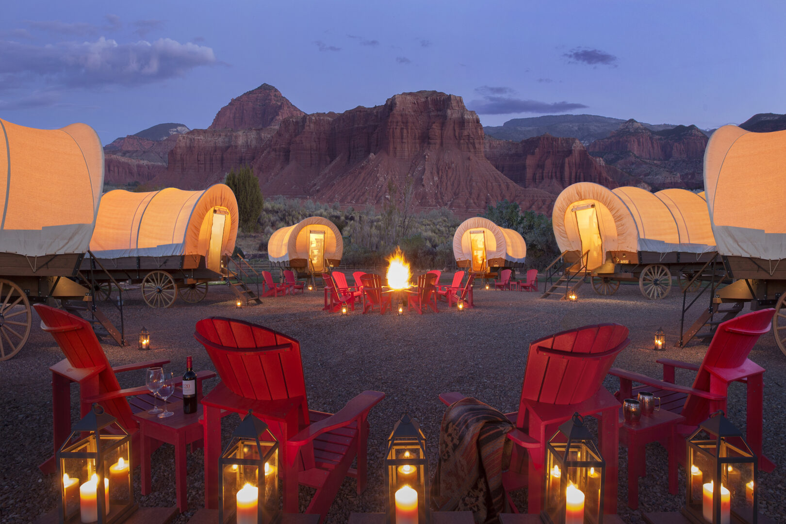 Conestoga covered wagons around a campfire in the evening with the mountains in the backdrop
